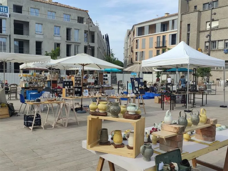 Marché en plein air à Antibes, avec des stands de produits artisanaux sous des parasols, entouré de bâtiments modernes.