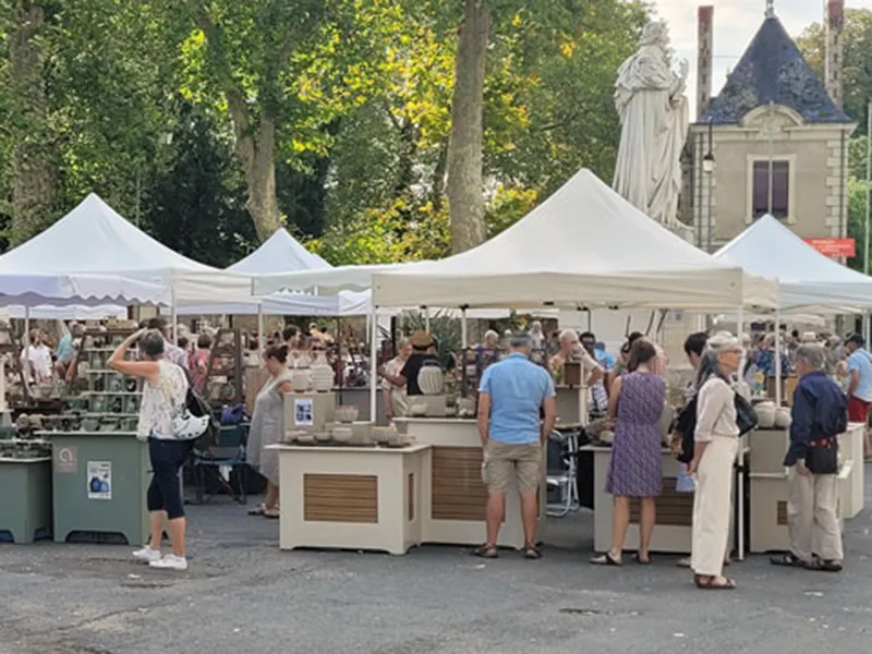 Marché animé avec des stands sous des tentes blanches, des visiteurs explorant des objets artisanaux en plein air.