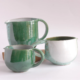Créations en céramique artisanale, trois pichets émaillés aux teintes vertes et blanches, élégance contemporaine.