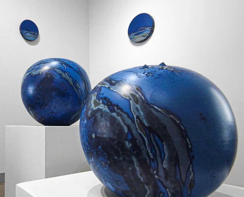 Sculptures en céramique aux teintes bleu profond, affichant des motifs fluides et modernes, exposition artistique contemporaine.