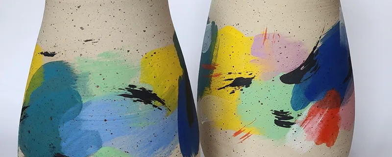 Vases en céramique aux couleurs vibrantes, décorés de touches de peinture abstraite sur fond beige.