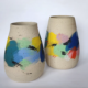 Vases en céramique aux couleurs vibrantes, décorés de touches de peinture abstraite sur fond beige.