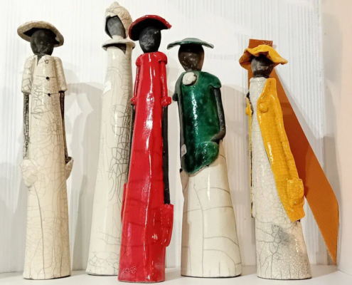 Sculptures en céramique colorée représentant des silhouettes élégantes, exposées dans un cadre artistique convivial.