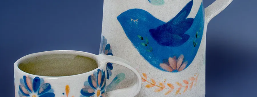 Pichet et tasse en céramique émaillée, décor floral coloré, création artisanale raffinée et joyeuse.