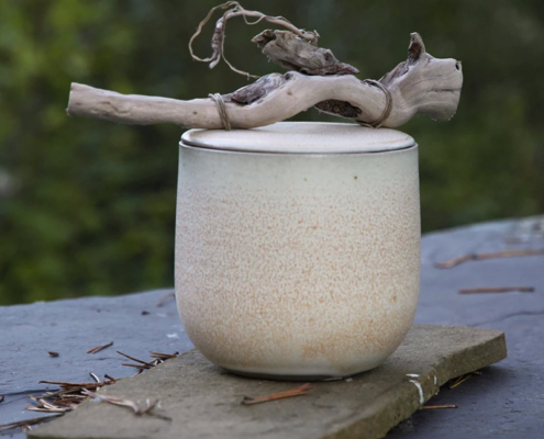 Récipient en céramique artisanale, émaillé aux teintes naturelles, avec une touche organique grâce à une branche décorative.