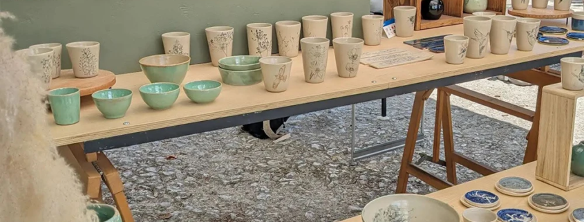 Stand d'artisans présentant des créations en céramique émaillée, ambiance conviviale au marché.