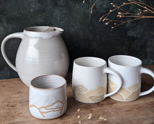 Pichets et mugs en céramique artisanale, décor géométrique sobre, créant une ambiance chaleureuse et élégante.