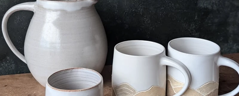 Pichets et mugs en céramique artisanale, décor géométrique sobre, créant une ambiance chaleureuse et élégante.