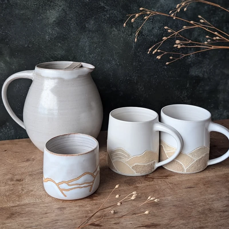 Pichets et mugs en céramique artisanale, décor géométrique sobre, créant une ambiance chaleureuse et élégante.